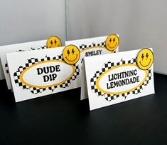 three signs with smiley faces on them are sitting on a black tablecloth covered surface