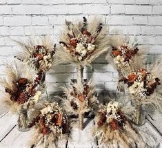 an arrangement of dried flowers and feathers arranged in a circle on a wooden table next to a brick wall