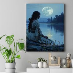 a woman sitting on the ground in front of a lake with a full moon behind her