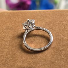 a diamond ring sitting on top of a cardboard box with flowers in the back ground