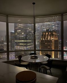 a table and chairs are in front of large windows overlooking the city lights at night