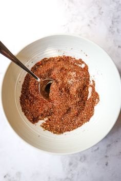 a white bowl filled with seasoning on top of a marble counter next to a wooden spoon