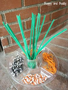 a plastic container filled with orange and green straws on top of a sidewalk next to a brick wall