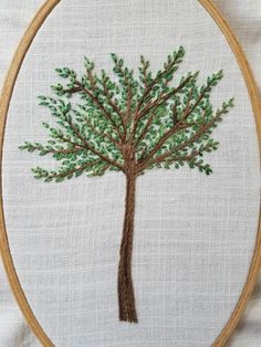 a cross stitched tree with green leaves on it's branches in a hoop