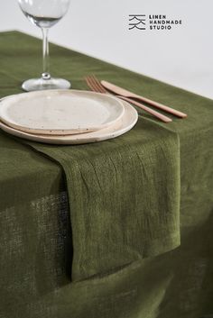 an empty plate on a green table cloth next to a wine glass and utensils