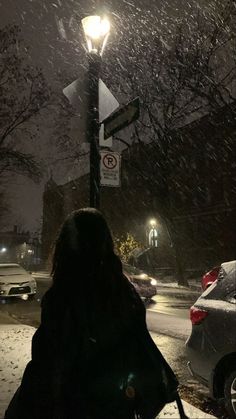 a woman walking down the street at night in the snow with her back to the camera