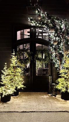 christmas trees are lit up in front of a house with lights on the door and windows