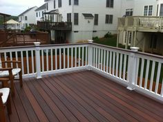 a wooden deck with white railings and chairs on the other side in front of some houses