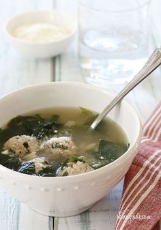 a bowl of soup with meatballs and spinach in it on a wooden table