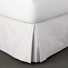 a white bed skirt with pleated edges on the bottom and bottom edge, in a bedroom