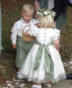 two young children dressed in white and green outfits, one holding a basket while the other holds