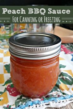 a mason jar filled with peach bbq sauce sitting on top of a tablecloth