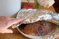 a person holding onto a piece of bread wrapped in aluminum foil on a table next to flowers