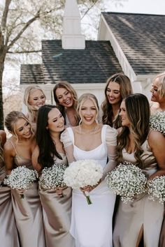 a group of women standing next to each other in front of a building holding bouquets