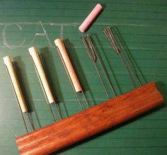 several different types of knitting needles on a green board with writing in chalk and crochet hooks