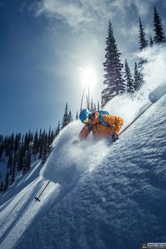 a man riding skis down the side of a snow covered slope with trees in the background