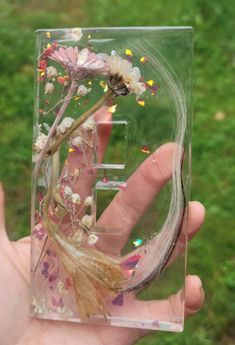 a hand holding a glass block with flowers in it