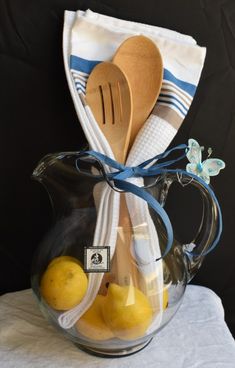 a glass pitcher filled with lemons and wooden spoons on top of a white towel