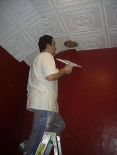 a man standing on a step ladder painting the ceiling with white paint and red walls