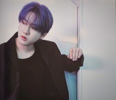 a young man with purple hair is leaning against a wall