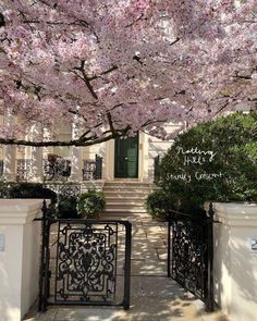 the entrance to an apartment building with pink flowers on trees and bushes in front of it