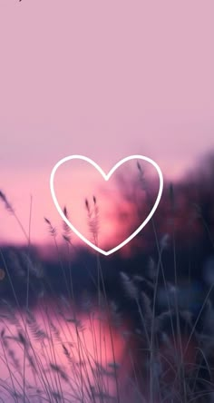 a white heart in the middle of some tall grass with pink and blue sky behind it