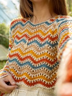 a woman wearing a multicolored crochet sweater and holding an orange object in her hand