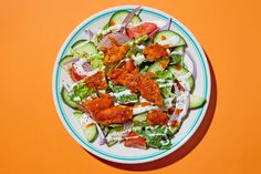 a white plate topped with lots of salad next to an orange wall and a fork