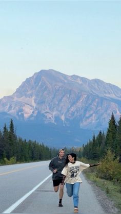 two people running down the road in front of a mountain