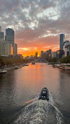 a boat is traveling down the river in front of a cityscape at sunset