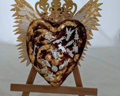 a heart shaped object with gold wings on a wooden stand