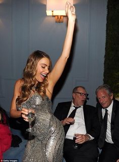 a woman in a silver dress is holding her arm up with two men sitting behind her