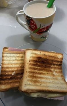 two grilled sandwiches on a glass plate with a cup of coffee in the background