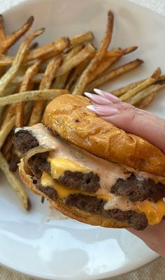 a hand holding a cheeseburger and french fries on a white plate with a napkin