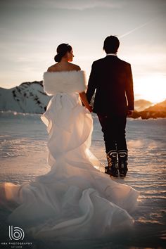 a bride and groom walking in the snow at sunset with their arms around each other