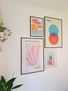 three framed posters hang on the wall next to a potted plant and a vase