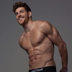 a shirtless man with his hands on his hips smiling at the camera while wearing boxer shorts