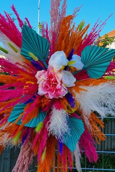 an arrangement of colorful feathers and flowers on a pole in front of a fenced area