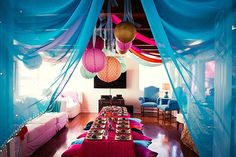 a long table is covered with blue sheer curtains and paper lanterns hanging from the ceiling