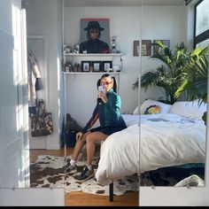 a woman sitting on a bed taking a selfie with her cell phone in the mirror