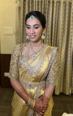 a woman in a gold sari and matching jewelry poses for the camera with her hands on her hips