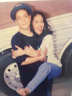 a man and woman hugging each other in front of a large tire with their arms around each other