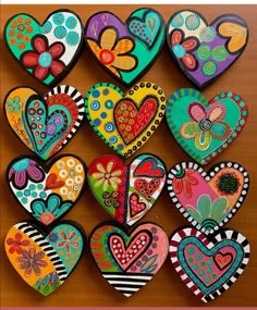 many colorful hearts are arranged on a wooden table with flowers and butterflies painted on them