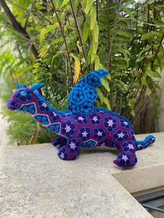 a purple and blue horse sitting on top of a cement slab next to plants in the background