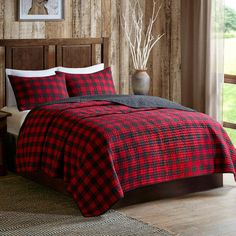 a red and black plaid comforter set on a bed in a room with wood paneling