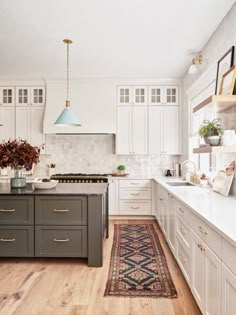 a large kitchen with white cabinets and wooden flooring, along with a rug on the floor