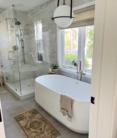 a large white bathtub sitting next to a window in a bathroom with a rug on the floor