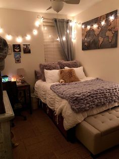 a bed with pillows and blankets on top of it next to a window covered in lights