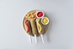 three crocheted hot dogs on a plate with dipping sauces