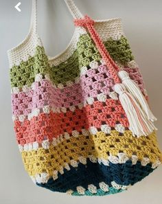 a multicolored crocheted bag hanging from a hook on a wall with a tassel